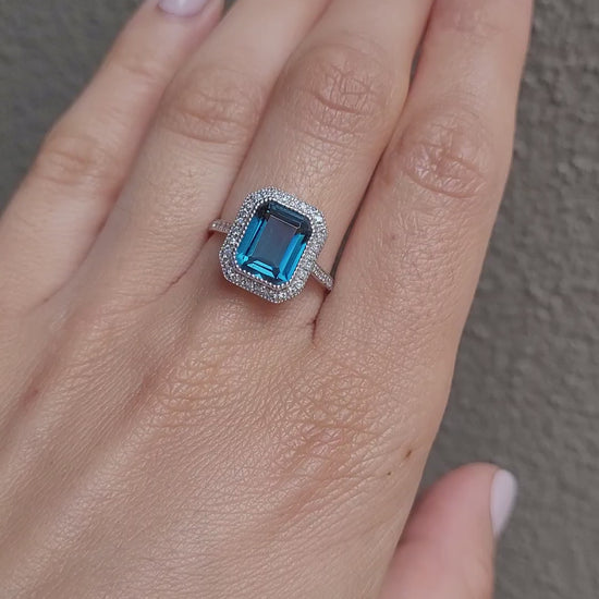 video on hand of white gold ring with London blue topaz and diamond halo in gray background