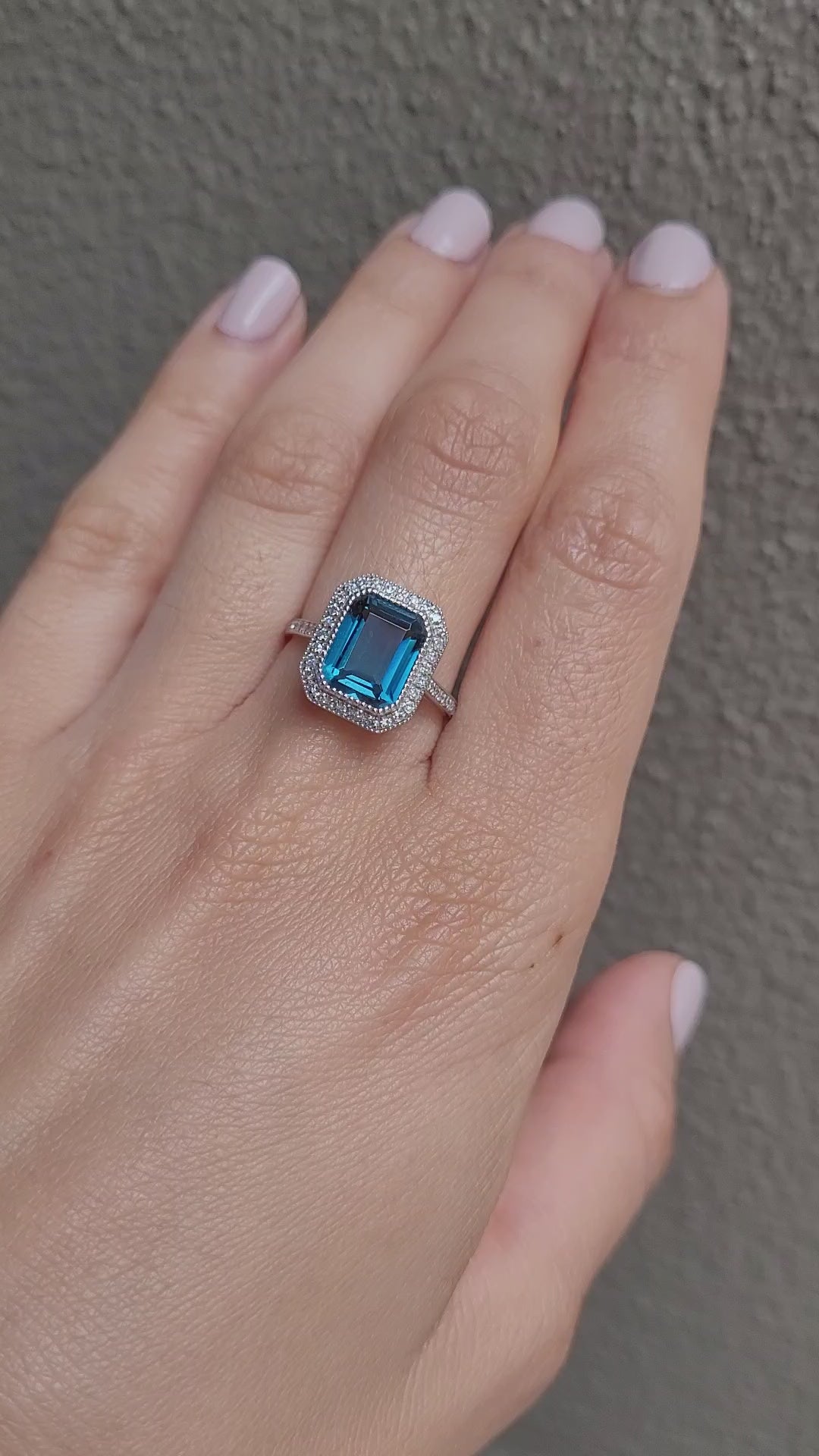video on hand of white gold ring with London blue topaz and diamond halo in gray background
