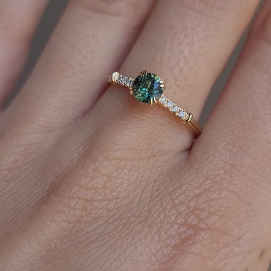 video on hand of Round Australian Teal Sapphire Ring with Diamond Band in neutral background
