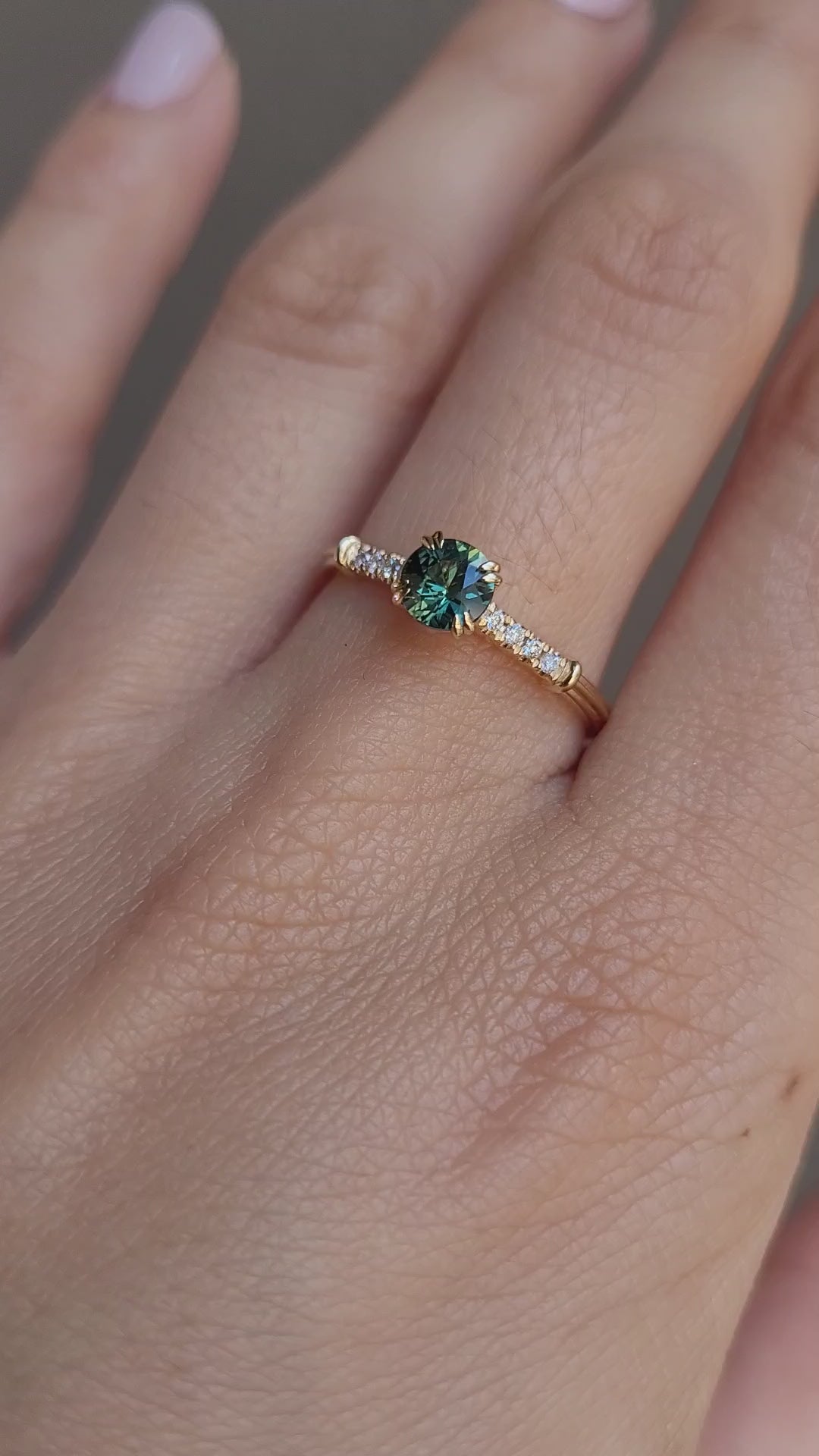 video on hand of Round Australian Teal Sapphire Ring with Diamond Band in neutral background