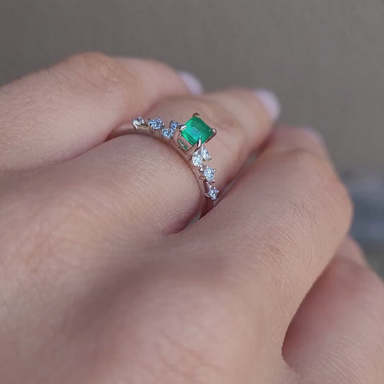 video on hand of platinum ring with emerald and diamonds in gray background