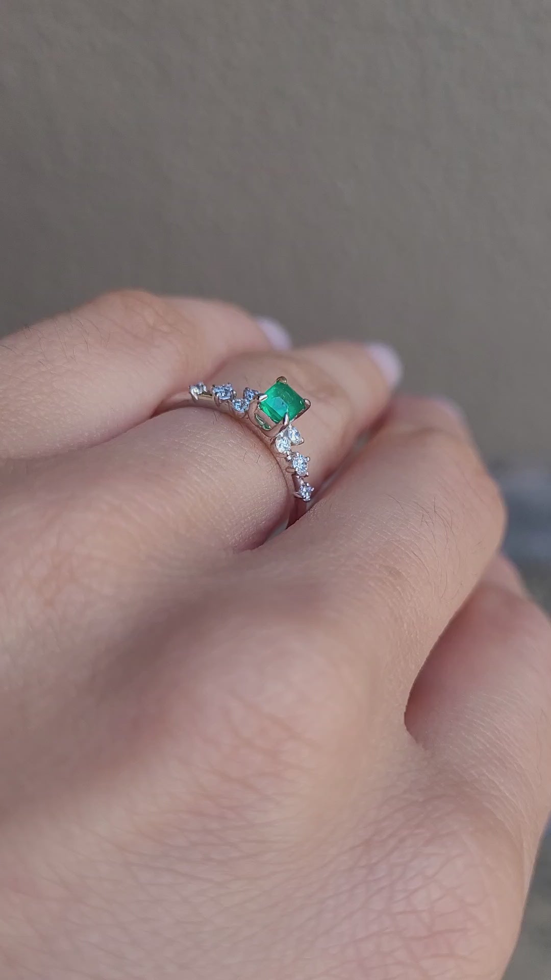 video on hand of platinum ring with emerald and diamonds in gray background