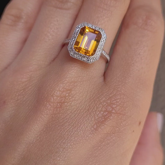 video on hand of Citrine and diamond halo ring in 18K white gold in light gray background