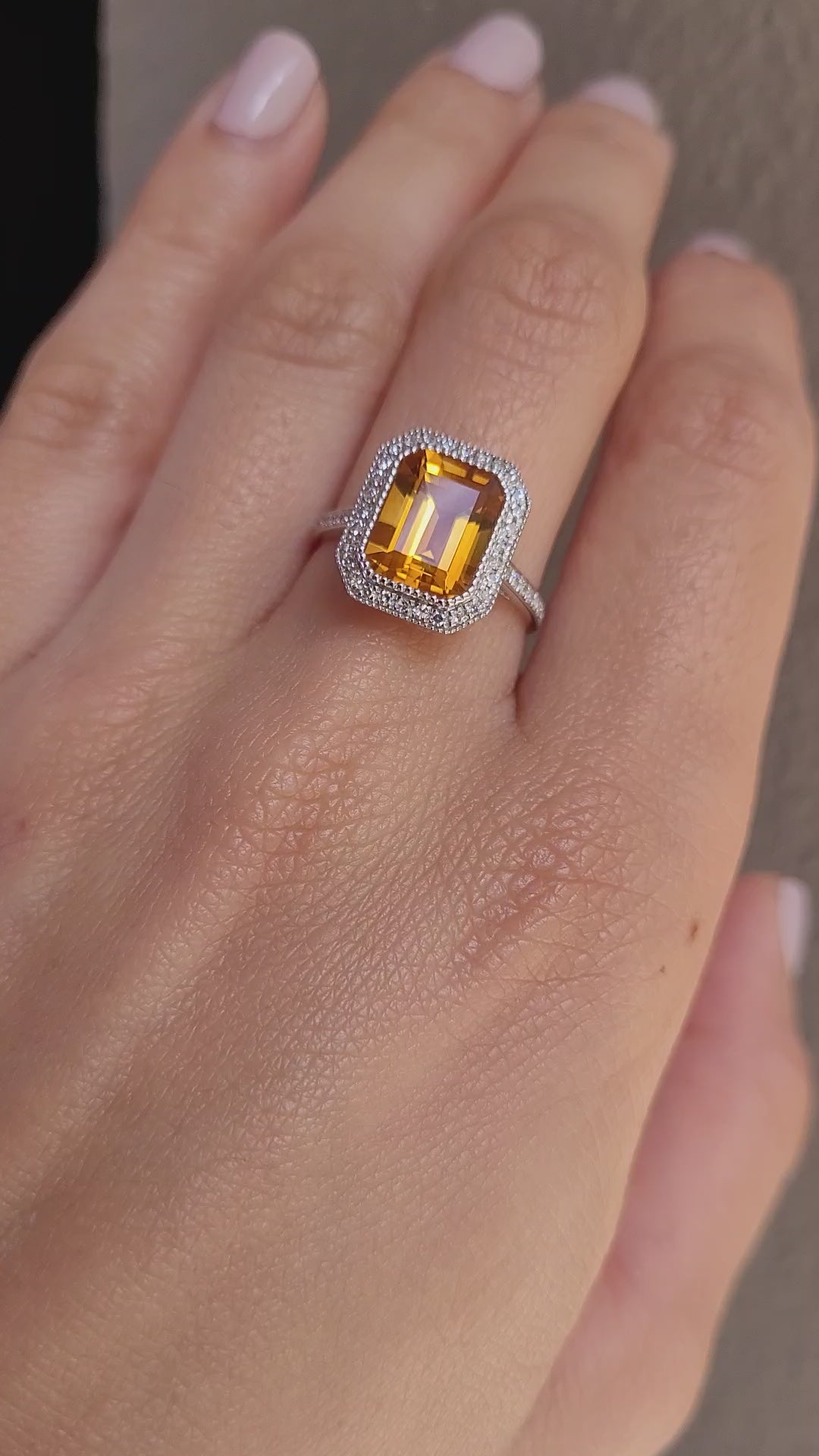 video on hand of Citrine and diamond halo ring in 18K white gold in light gray background