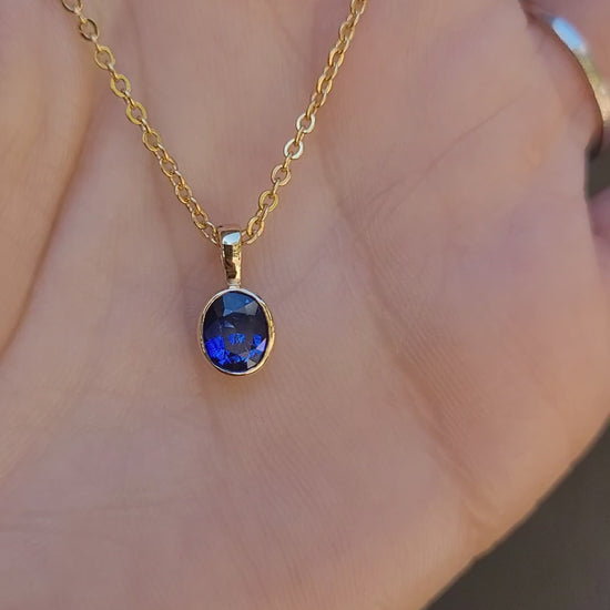 video of Royal Blue Sapphire Pendant in 18K Yellow Gold held in hand in neutral background