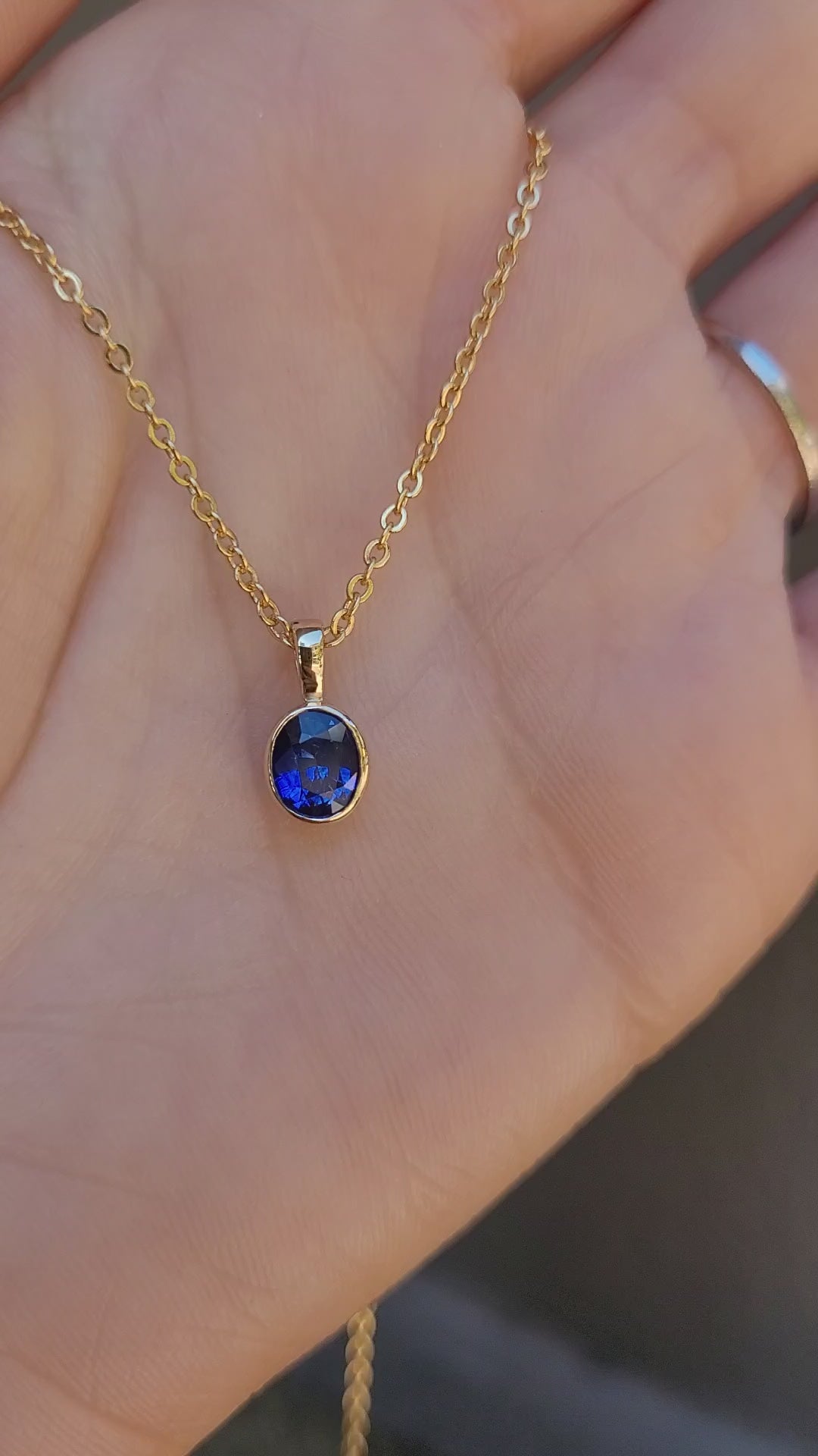 video of Royal Blue Sapphire Pendant in 18K Yellow Gold held in hand in neutral background