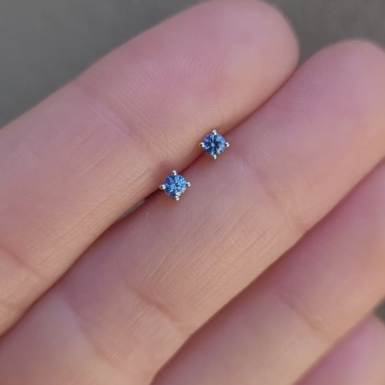video of small natural blue sapphire platinum earring held between fingers against a neutral background