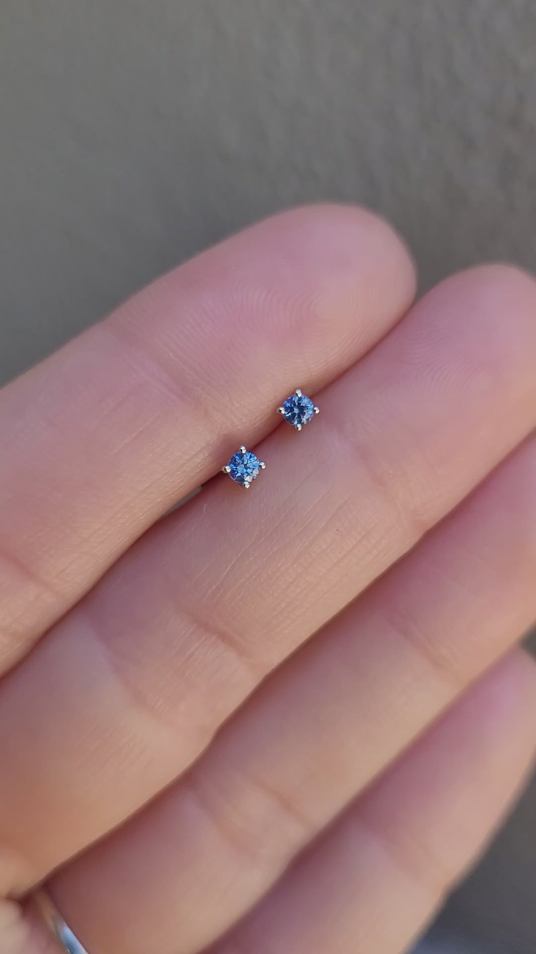 video of small natural blue sapphire platinum earring held between fingers against a neutral background
