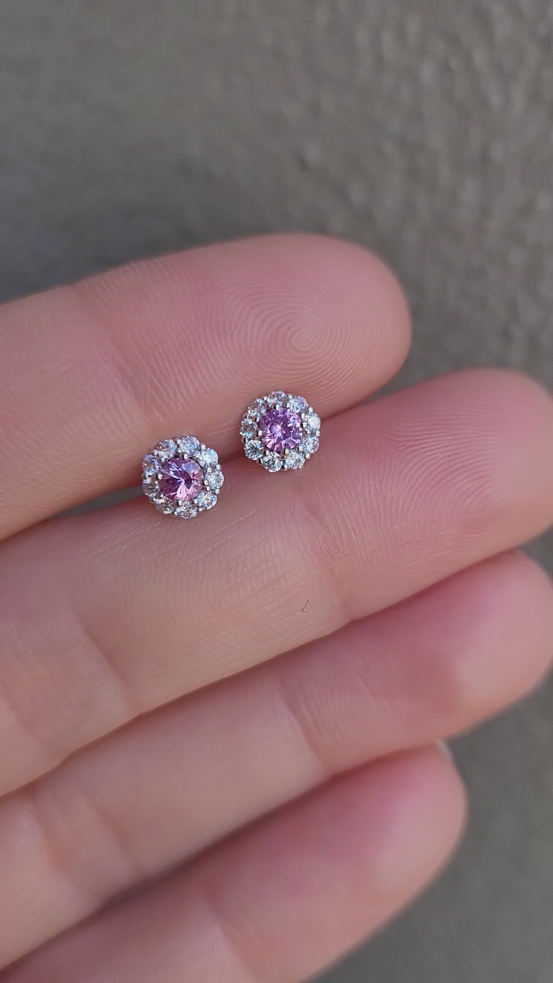 video of a pair of pink sapphire earrings held between fingers against a neutral background