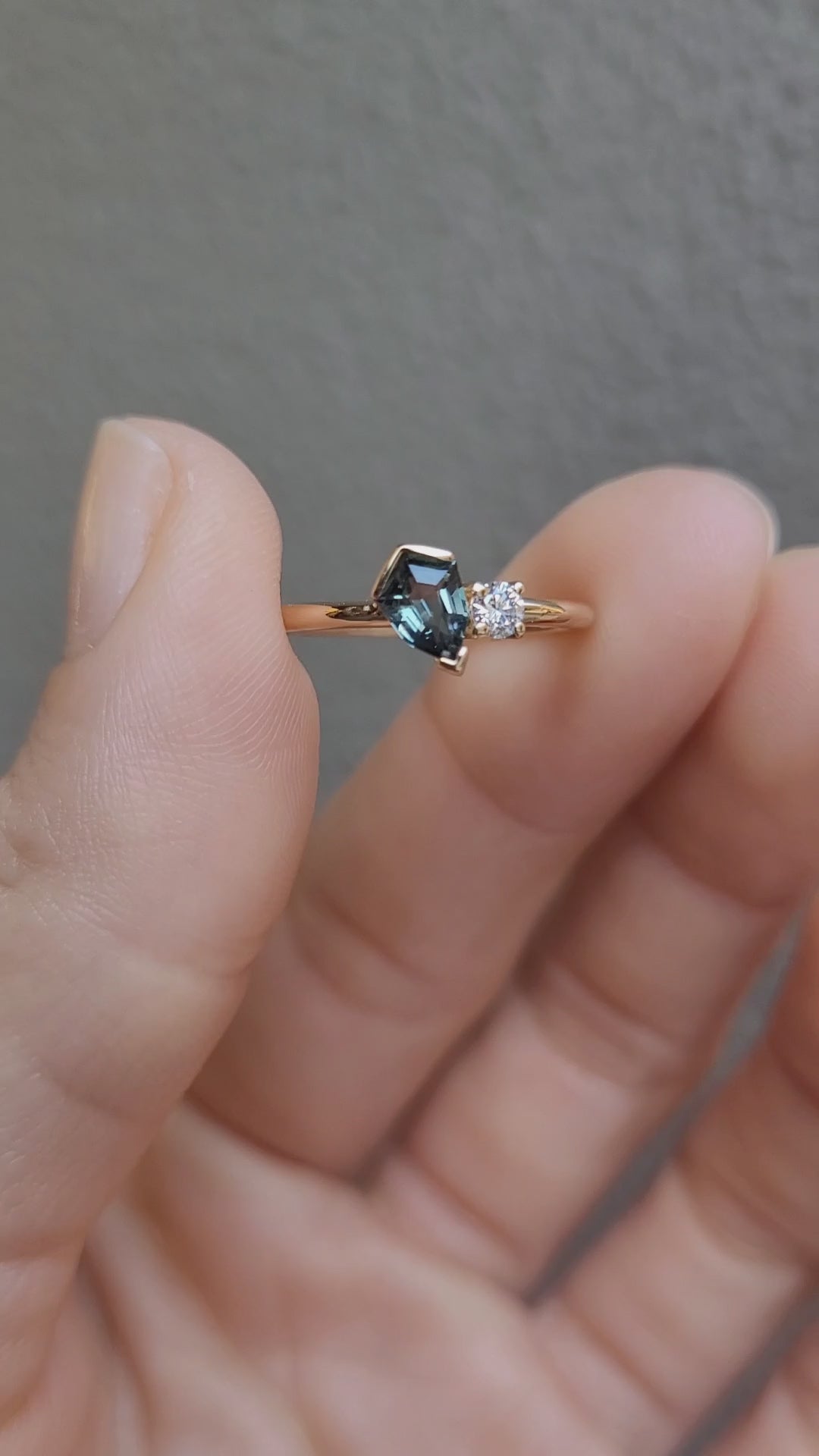 video of Teal Sapphire and Diamond Toi et Moi Ring in 18K Yellow Gold held between fingers in neutral background 