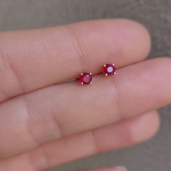 video of 18K Gold stud earrings with ruby gemstones on a person's finger against a neutral background