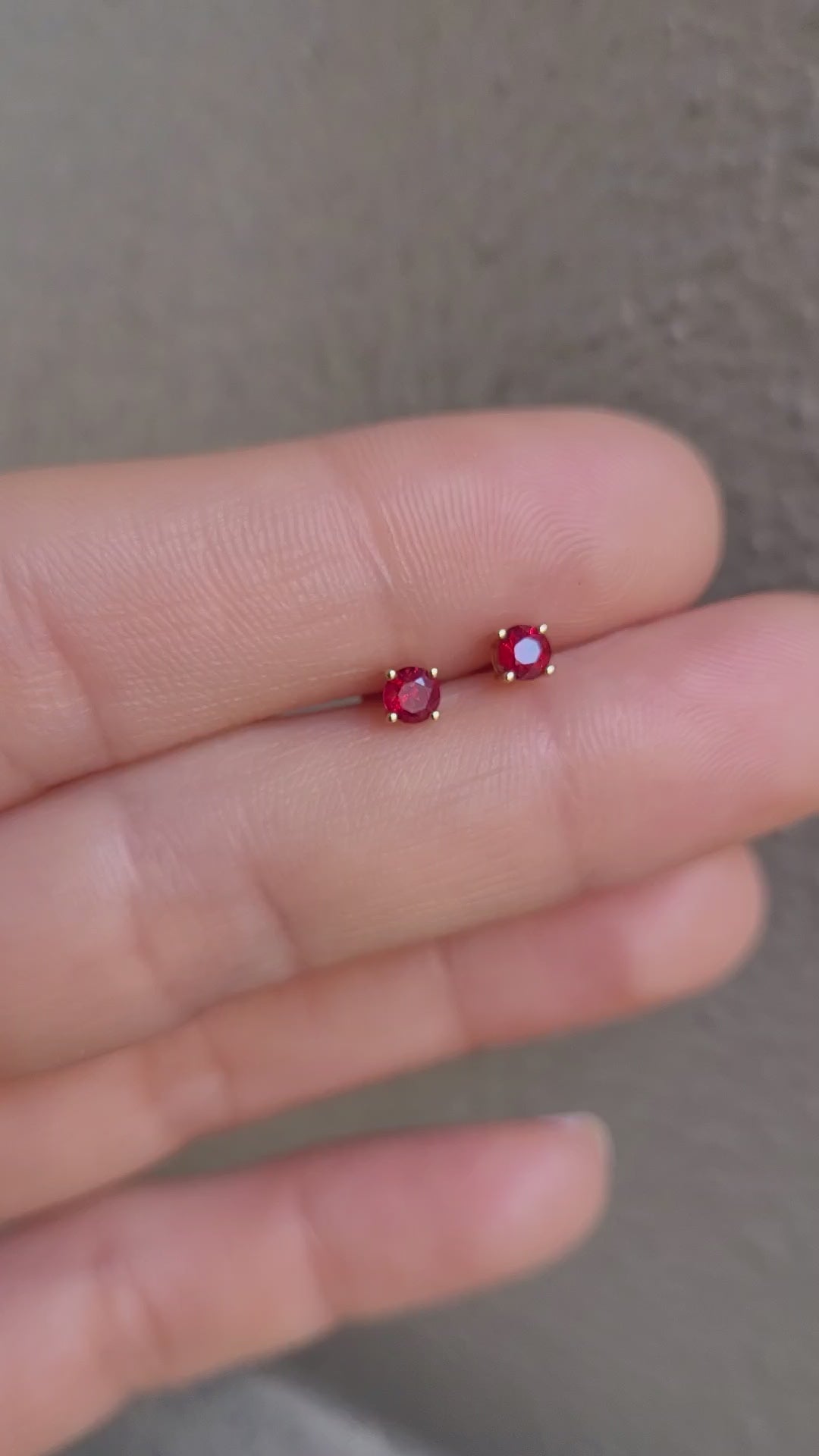 video of 18K Gold stud earrings with ruby gemstones on a person's finger against a neutral background