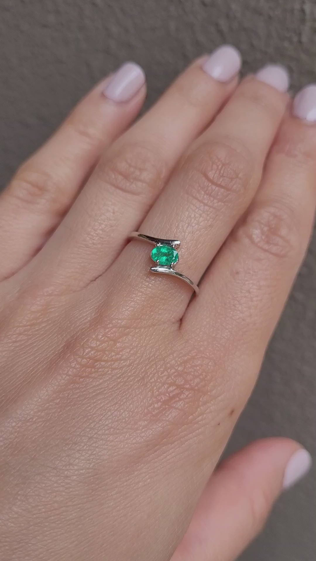 video on hand of white gold ring with natural Colombian emerald in light gray background