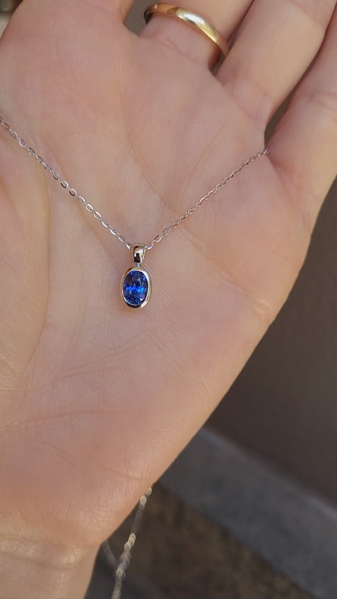 video of platinum pendant with blue sapphire held on hand