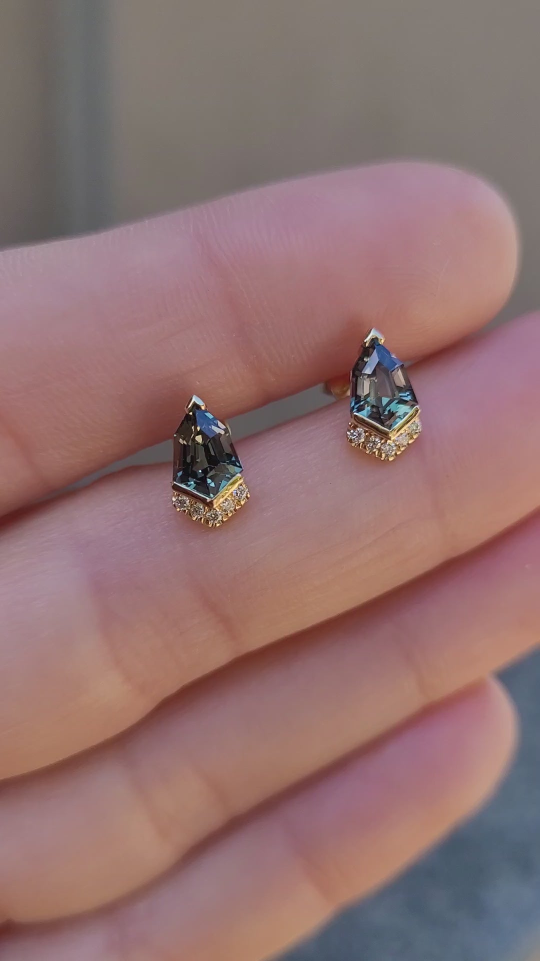 video of Shield Cut Teal Sapphire Diamond Stud Earrings in 18K Yellow Gold held in between fingers
