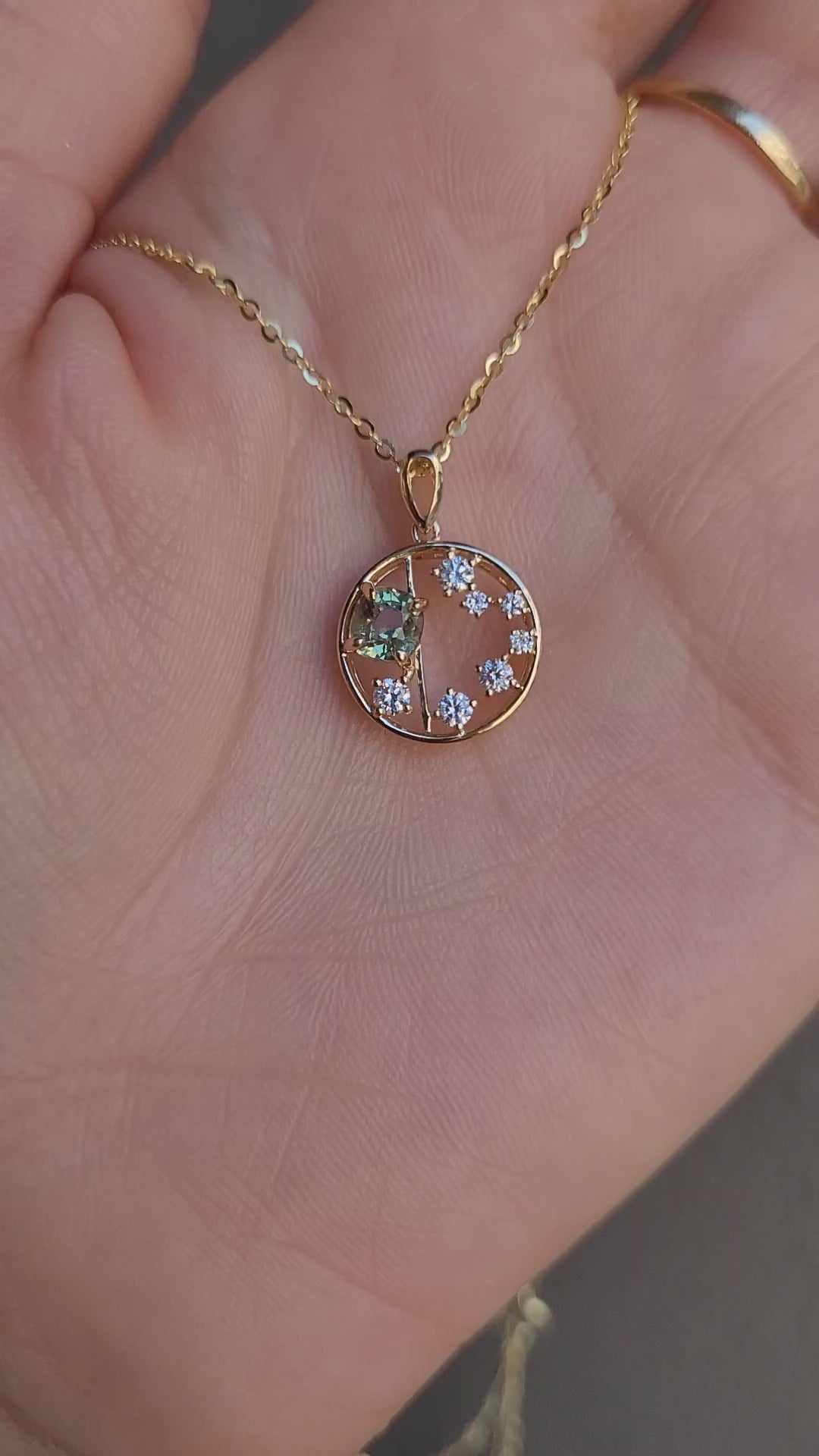 video of open circle gold pendant with alexandrite gemstone and small diamonds on a hand