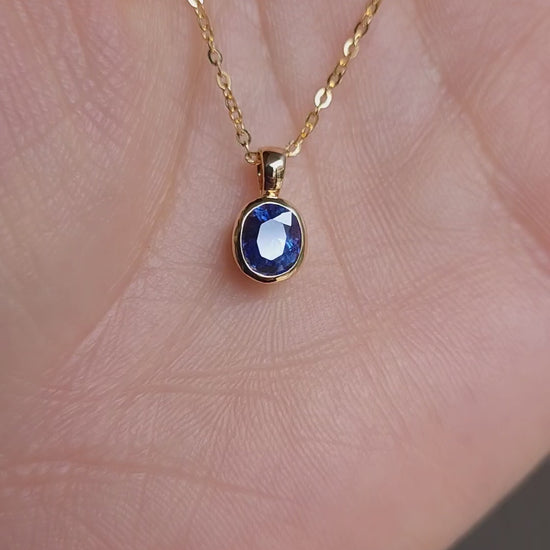 video gold pendant with a blue sapphire held in hand