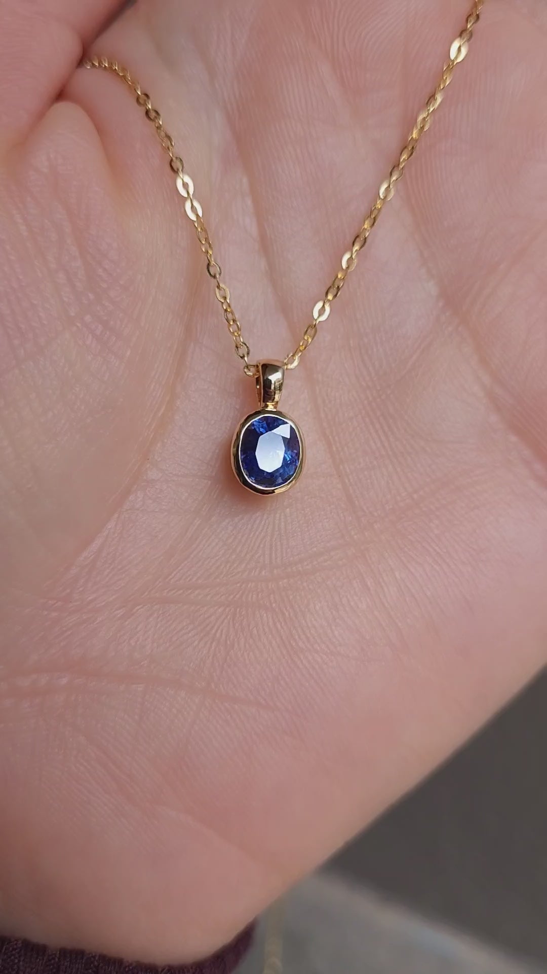 video gold pendant with a blue sapphire held in hand