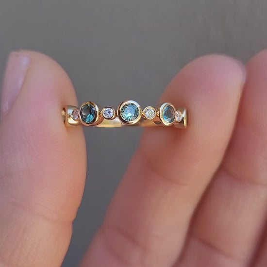 close-up video of a half eternity band featuring five round Australian teal sapphires and five small diamonds accent stones, set against a clean white background with a soft reflection.