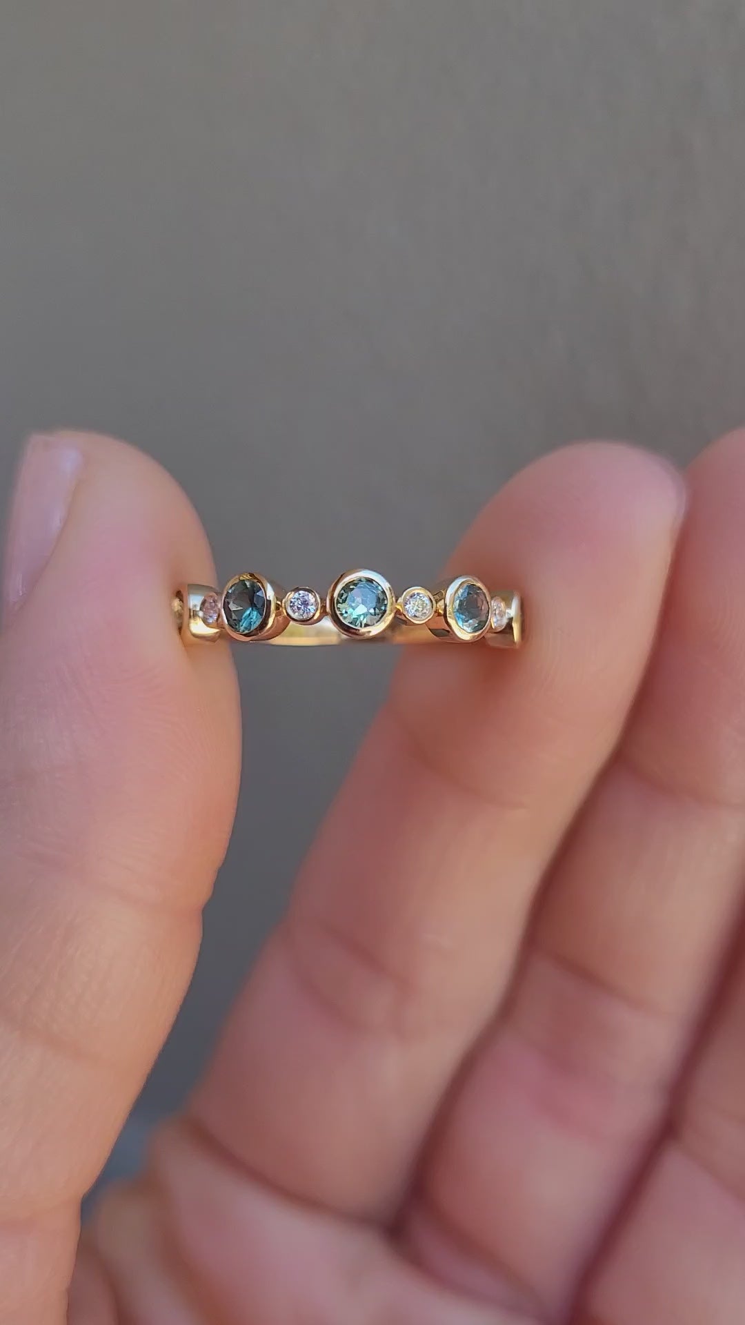 close-up video of a half eternity band featuring five round Australian teal sapphires and five small diamonds accent stones, set against a clean white background with a soft reflection.