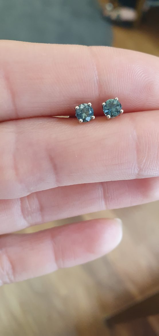 view on hand displaying a lighter colour of Australian Teal Sapphire Stud Earrings in 18K White Gold – 0.58ct Round Cut - 1982779