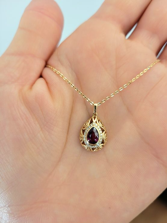 photo on hand of Pear Shape Unheated Ruby Pendant with Diamond Halo in Elegant Drop Design