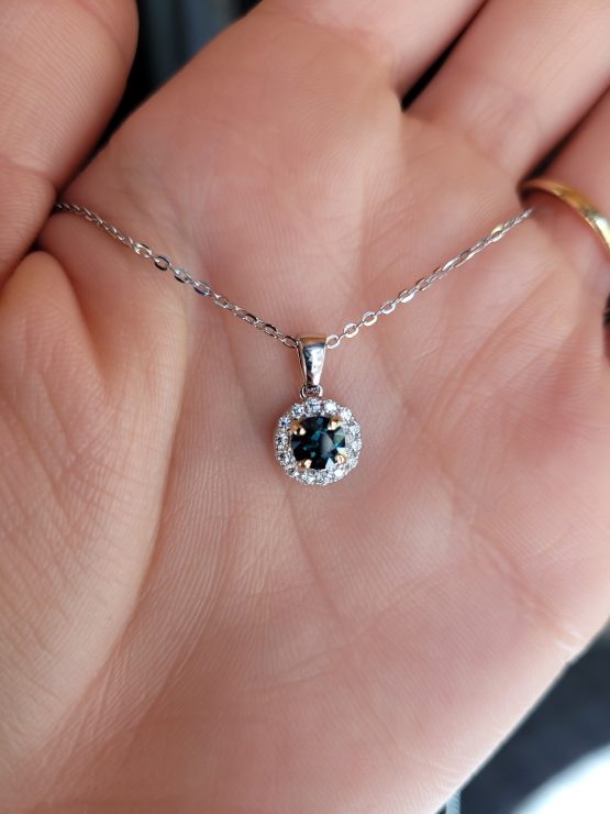 photo of hand of 0.64ct Australian Teal Sapphire & Moissanite Halo Pendant in 9K White Gold